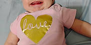Macie joined the competition — help win amazing prizes! arm, baby, bed, child, closeup, cute, expression, face, gold_heart, happy, indoors, infant, joy, love_text, lying_down, pink_onesie, skin, smiling, soft_surface, toddler