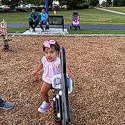 Antonella is registered to the contest to win money with this photo: adults, bench, casual_clothing, child, daylight, family, fun, grass, outdoor, park, people, pink_bow, pink_shoes, play, playground, spring_rocker, stroller, toddler, trees, wood_chips