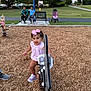 adults, bench, casual_clothing, child, daylight, family, fun, grass, outdoor, park, people, pink_bow, pink_shoes, play, playground, spring_rocker, stroller, toddler, trees, wood_chips