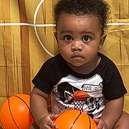 Nico joined the competition — help win amazing prizes! toddler, child, basketball, toy, curly_hair, black_hair, black_tshirt, sitting, indoor, yellow_background, orange, person, young_child, cute, portrait, serious_expression, baby, sport, ball, hands
