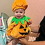 baby, bed, blanket, celebration, child, costume, cozy, cute, festive, green, halloween, happy, holding, indoor, infant, orange, person, pillow, pumpkin_costume, smile