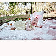 Oaklynn joined the competition — help win amazing prizes! baby, child, toddler, outdoor, blanket, pink_bow, yellow_dress, smiling, happy, toy, pillow, grass, trees, sunlight, nature, cute, lying_down, infant, headband, forest