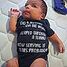 baby, infant, onesie, text_on_clothing, mattress, bedroom, controller, video_game_controller, purple, cute, lying_down, child, human, skin, hand, foot, expression, clothing, indoors, soft_light