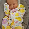 Melody is registered to the contest to win money with this photo: baby, infant, sleeping, newborn, portrait, face, floral_outfit, yellow_clothing, padded_seat, baby_carrier, striped_background, indoors, resting, peaceful, closed_eyes, head, arms, legs, photography, cute