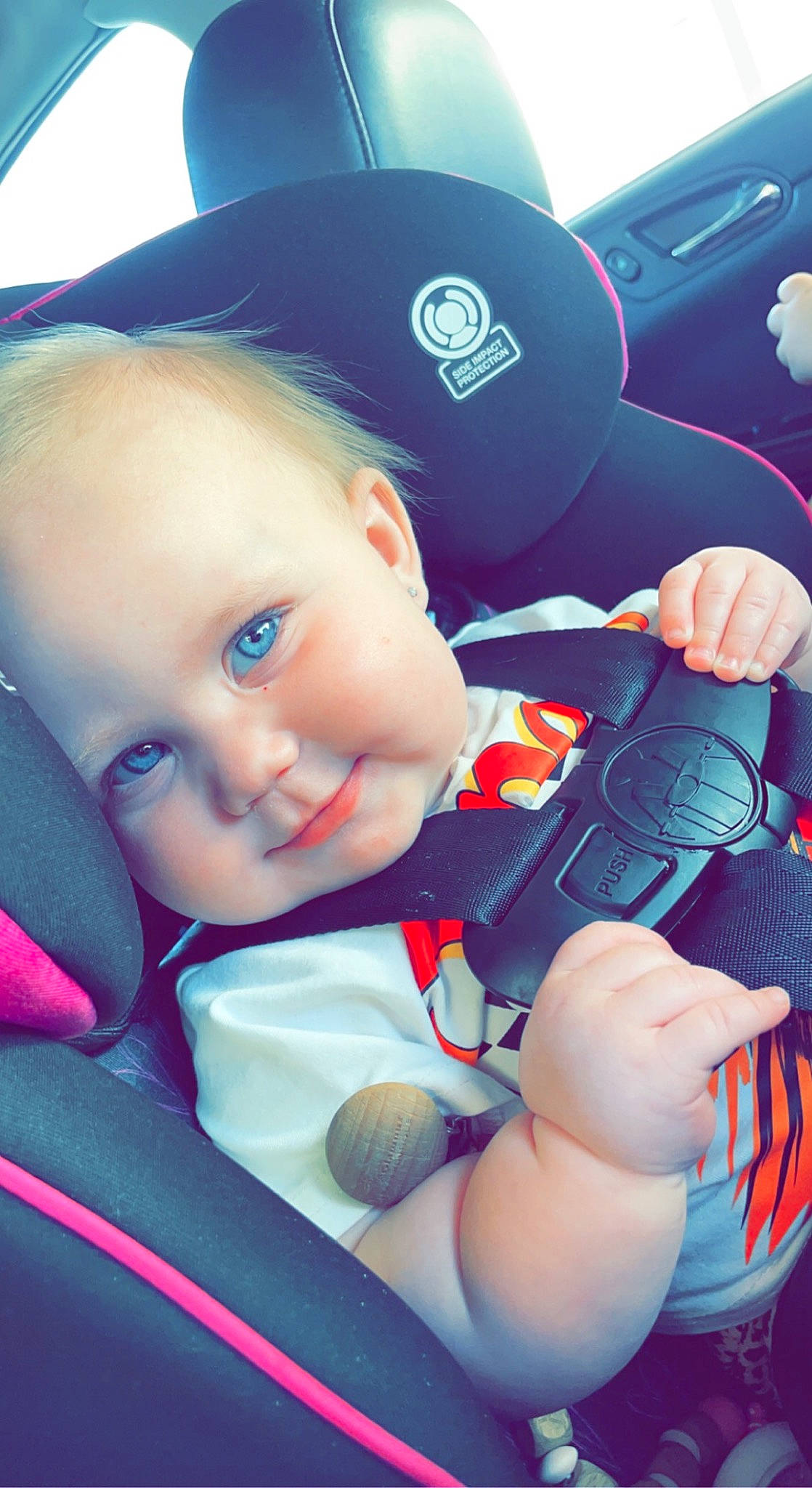 Brynlee is registered to the contest to win money with this photo: auto_part, automotive_design, azure, baby, baby_toddler_clothing, blue, car_seat, cool, eye, facial_expression, grass, happy, mammal, person, product, skin, smile, steering_part, steering_wheel, toddler