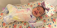 Skyla is registered to the contest to win money with this photo: baby, infant, smiling, onesie, tie_dye, headband, bow, crib, mesh, floral, mattress, sleepwear, cute, child, indoor, person, happy, lying_down, pattern, soft