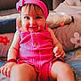 Carla is registered to the contest to win money with this photo: baby, child, pink_clothing, headband, smiling, sitting, indoors, cushion, blanket, happy, person, cute, infant, closeup, portrait, bright_colors, playful, cozy, home, warm_lighting