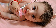 Carla is registered to the contest to win money with this photo: baby, pacifier, pink_cloth, bracelet, necklace, infant, cute, lying_down, indoor, person, face, hand, curious, close_up, soft_lighting, blurred_background, family, child, skin, hair