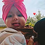 Carla is registered to the contest to win money with this photo: baby, child, smiling, pink_turban, flower_headwear, tongue_out, hand, adult, outdoor, greenery, blurred_background, happy, cute, portrait, close_up, headwear, person, infant, love_emoji, warm_clothing