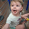 toddler, child, shopping_cart, toy_duck, green_hair_clip, playful, tongue_out, casual_clothing, shorts, white_shirt, indoor, store_floor, happy, cute, person, baby, retail, fun, smiling, expression