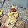 baby, child, bed, pillow, blanket, hat, clothing, infant, cute, pattern, cartoon, sleepwear, footwearless, indoors, person, lying_down, expression, young, soft_furnishing, cozy