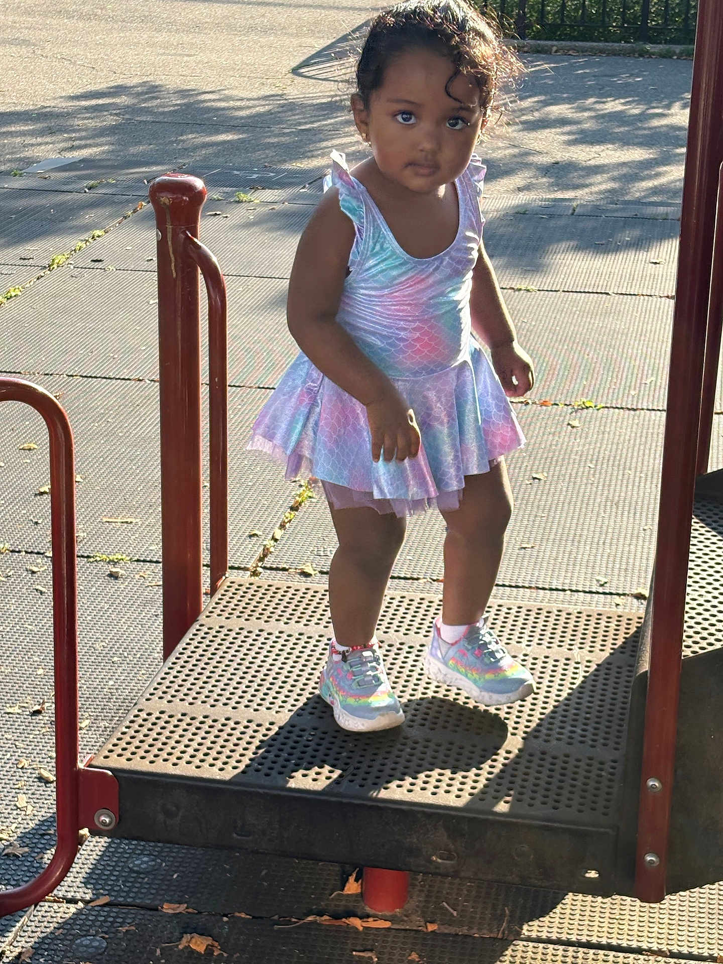 Zoey is registered to the contest to win money with this photo: child, girl, playground, dress, shoes, platform, outdoor, sunlight, shadow, curly_hair, person, casual_clothing, daylight, play_area, metal_structure, cute, young, standing, park, footwear