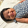baby, child, smile, face, blue_dress, floral_pattern, lying_down, bed, white_bed_sheet, infant, happy, skin, hair, arm, person, indoors, cute, young, portrait, sleepwear