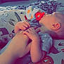 baby, hand, pacifier, blanket, animal_pattern, infant, bedroom, furniture, drawer, basket, clothing, person, holding_hands, lying_down, soft_lighting, toddler, comfort, indoor, sleepy, cuddle