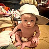 baby, cap, carpet, child, clutter, curious, doll, expression, face, floor, furniture, hat, home, indoors, looking, naked, person, sitting, small, toy
