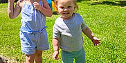 Sapphire joined the competition — help win amazing prizes! child, children, toddler, smiling, outdoor, grass, sunlight, summer, playful, curly_hair, romper, shorts, socks, backyard, tree, fence, happy, barefoot, greenery, daylight