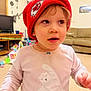 toddler, child, red_hat, sweater, polar_bear, indoor, living_room, toy, couch, television, furniture, carpet, cute, person, headwear, smiling, baby, young_child, room, casual