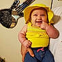 baby, child, smile, yellow_hat, yellow_top, denim_shorts, indoor, person, hand, mirror, guitar_shaped_mirror, wall, furniture, happy, cute, holding, portrait, infant, clothing, room