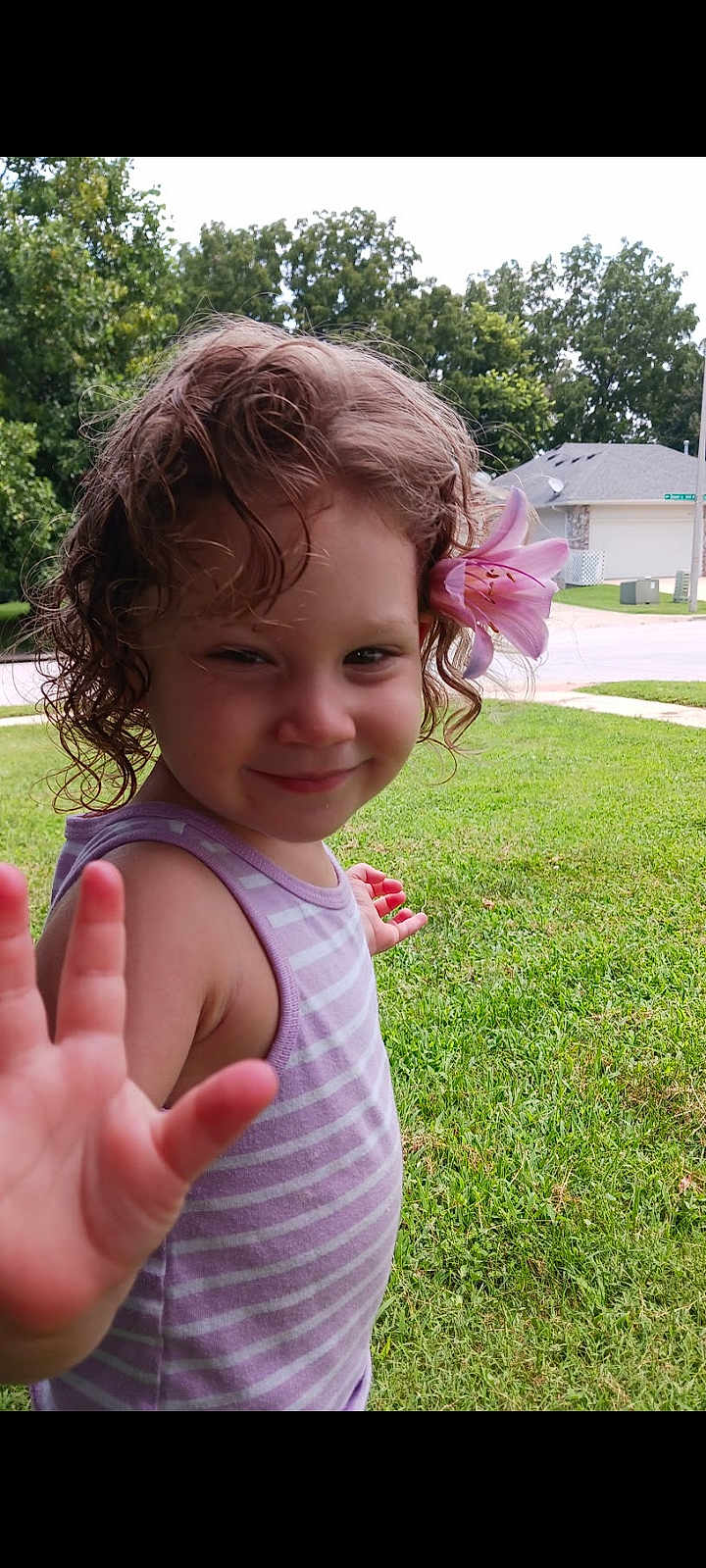 Ana'Leigh Rose joined the competition — help win amazing prizes! child, girl, curly_hair, flower, lily, smiling, waving_hand, outdoor, grass, trees, residential_area, summer, tank_top, purple_stripes, nature, cute, portrait, happy, daylight, person