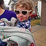 toddler, child, sunglasses, heart_shaped, blanket, curly_hair, outdoor, person, plaid_shirt, suburban, house, driveway, car, purple_shirt, cute, smile, holding, daylight, sidewalk, casual
