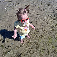 éloïse a rejoint le concours — aidez-le/la à gagner de superbes lots ! barefoot, beach, casual_clothing, child, cute, exploring, hair_tie, outdoor, pacifier, playful, sand, seaweed, shadow, shorts, summer, sunglasses, sunny, toddler, water, yellow_shirt