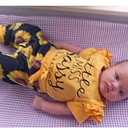 Raelynn is registered to the contest to win money with this photo: baby, infant, yellow_clothing, sunflower_pattern, purple_checkered, lying_down, child, cute, face, portrait, short_sleeves, pants, soft_surface, young_child, looking_at_camera, indoors, casual, comfortable, resting, baby_girl