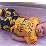 baby, infant, yellow_clothing, sunflower_pattern, purple_checkered, lying_down, child, cute, face, portrait, short_sleeves, pants, soft_surface, young_child, looking_at_camera, indoors, casual, comfortable, resting, baby_girl