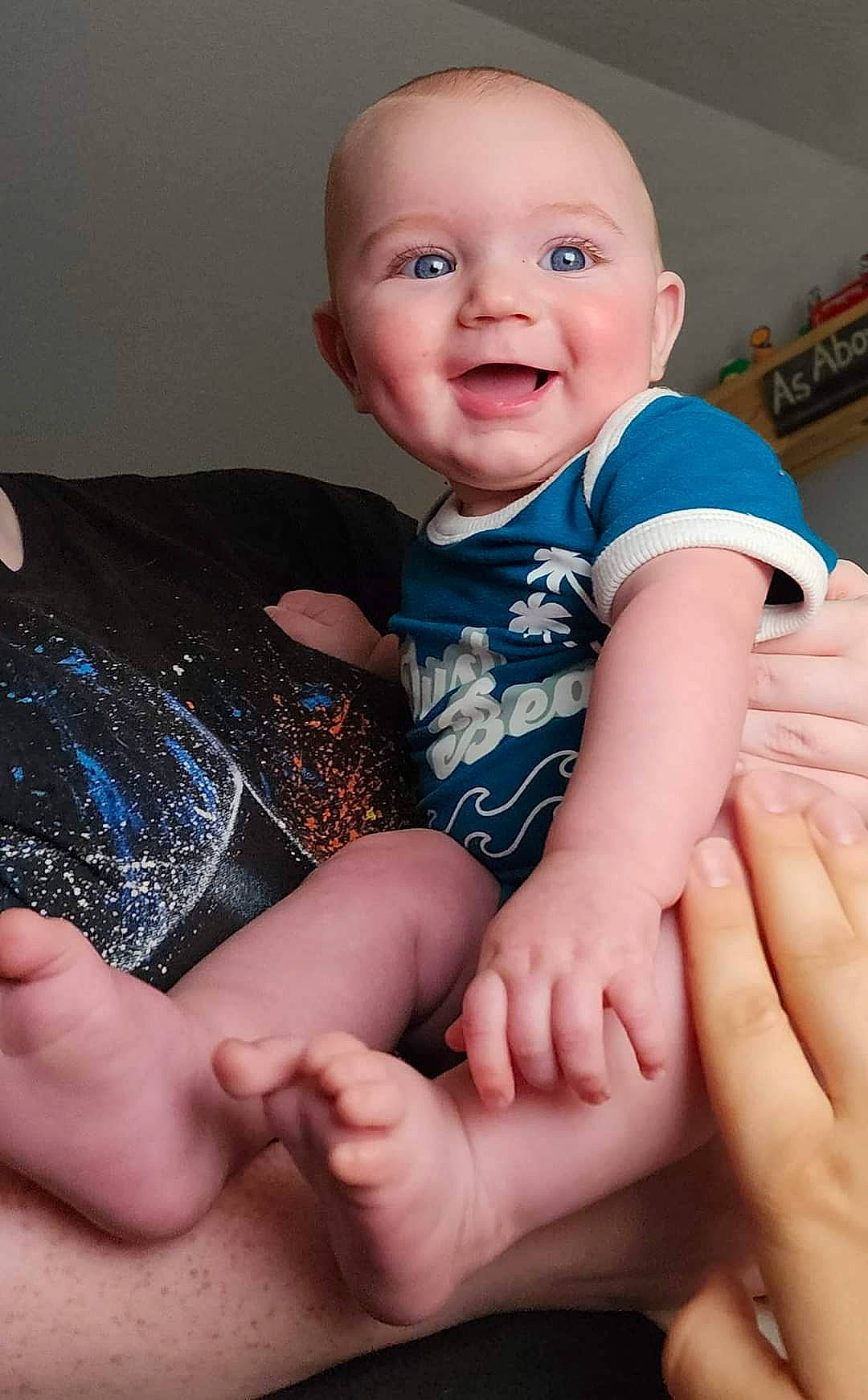 Damian is registered to the contest to win money with this photo: arm, baby_toddler_clothing, cheek, comfort, eye, finger, gesture, hand, head, human_body, joint, joy, leg, muscle, neck, person, shoulder, skin, sleeve, smile