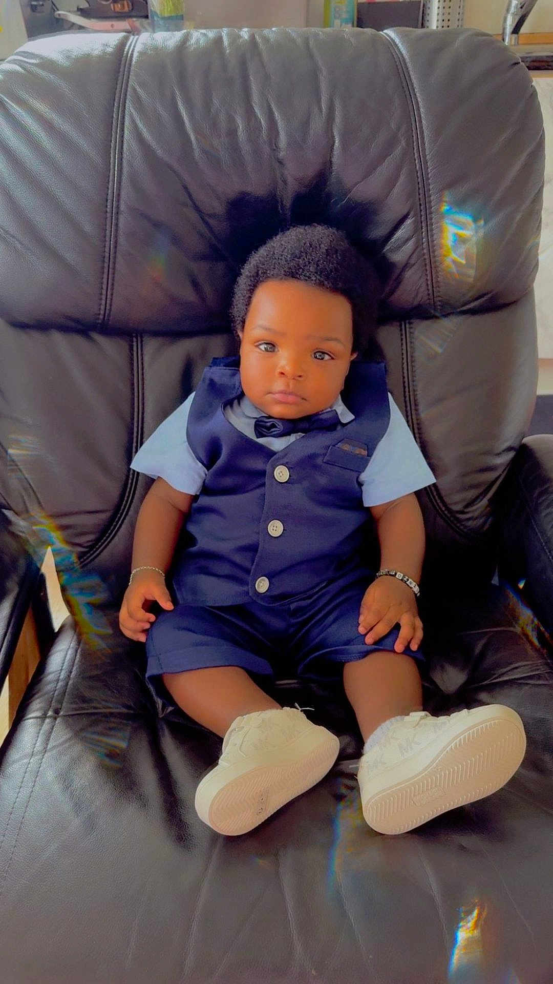 Uriel David a rejoint le concours — aidez-le/la à gagner de superbes lots ! baby, child, infant, person, sitting, leather_chair, indoor, clothing, vest, shorts, white_shoes, bracelet, cute, portrait, looking_at_camera, black_hair, comfortable, furniture, calm, young