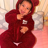 Melody joined the competition — help win amazing prizes! adorable, baby, bear_hood, bed, child, close_up, cloud_pattern, fuzzy_texture, happy, hooded_clothing, indoors, infant, nursery, pillow, portrait, red_outfit, sitting, smiling, tongue_out, toy