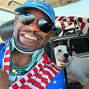 Wishbone joined the competition — help win amazing prizes! man, smiling, sunglasses, cap, dog, black_and_white_dog, car_interior, seat, seatbelt, jacket, stars_and_stripes, flag_pattern, pet, happy, portrait, reflection, window, daylight, face, animal