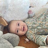 Ambre participe au concours pour gagner de l'argent avec cette photo : baby, infant, smiling, face, onesie, floral_pattern, pacifier, stuffed_animal, plush, soft_texture, child, cute, lying_down, happy, cozy, indoors, portrait, closeup, head, hand