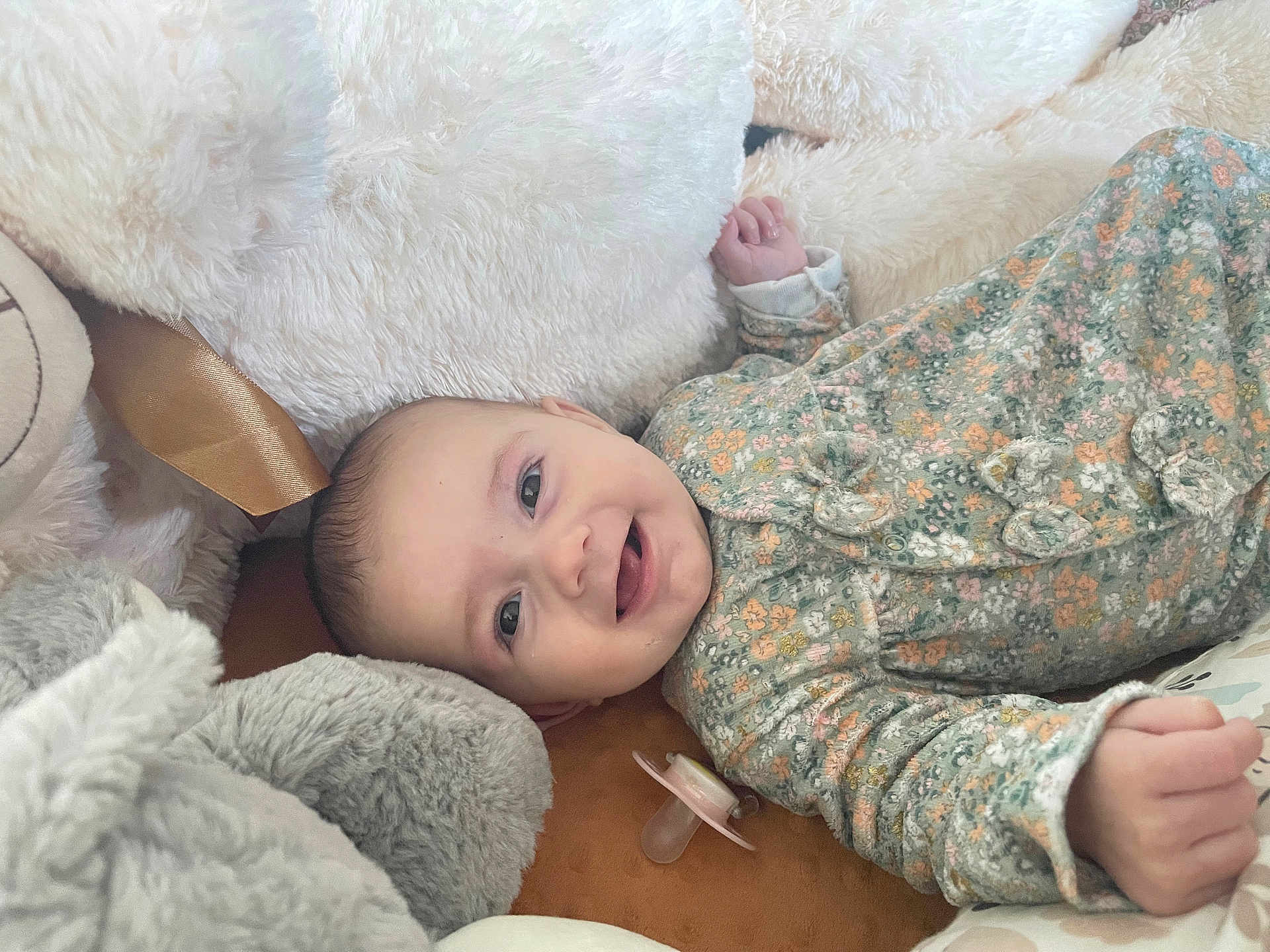 Ambre participe au concours pour gagner de l'argent avec cette photo : baby, infant, smiling, face, onesie, floral_pattern, pacifier, stuffed_animal, plush, soft_texture, child, cute, lying_down, happy, cozy, indoors, portrait, closeup, head, hand