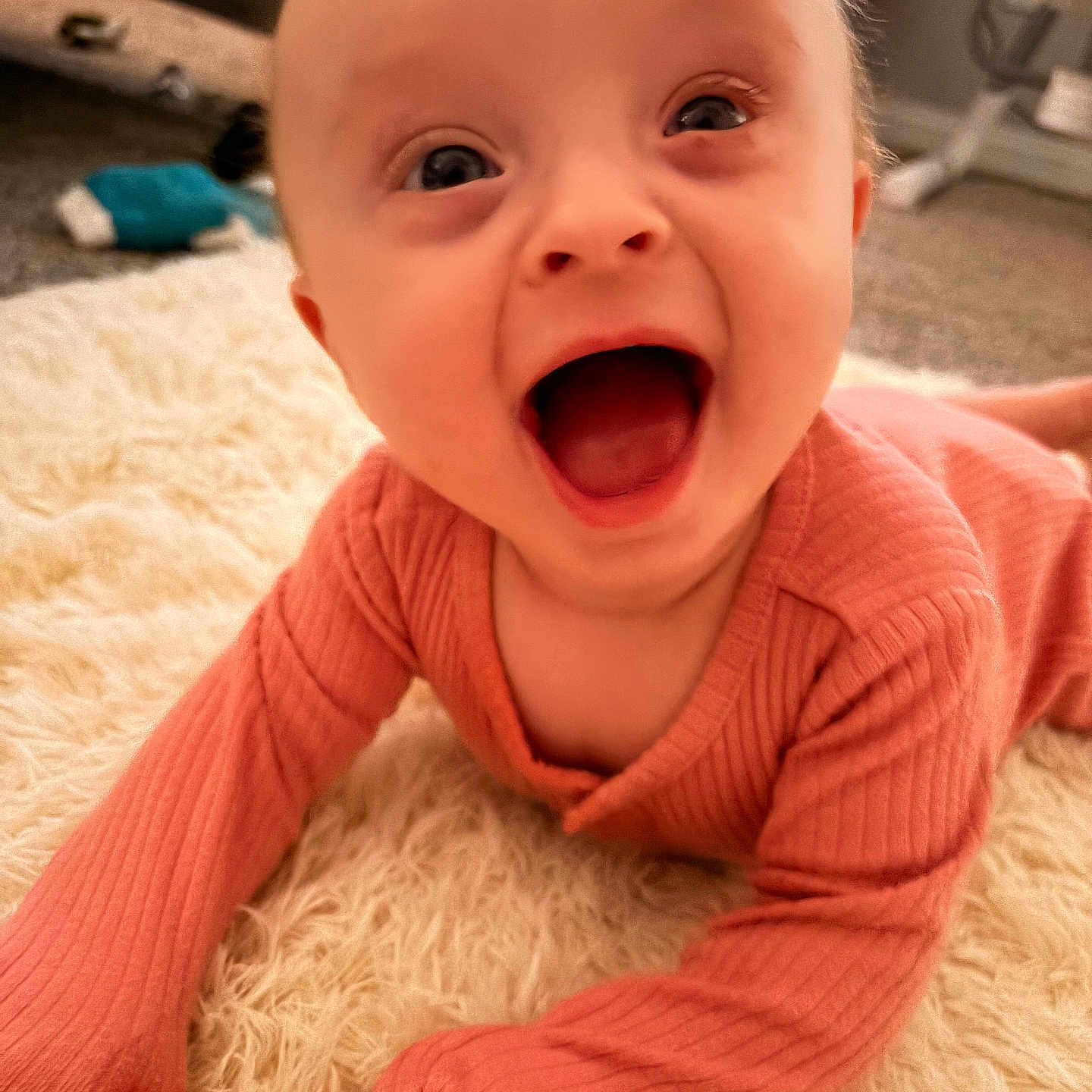 Alora is registered to the contest to win money with this photo: baby, infant, smiling, happy, mouth_open, pink_clothing, long_sleeves, lying_down, carpet, fluffy_rug, indoor, child, cute, portrait, person, young_child, head, face, expression, skin