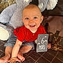 baby, infant, smiling, red_shirt, striped_shorts, plush_toy, koala, milestone_card, indoor, blanket, cushion, happy, child, cute, portrait, sitting, face, hand, feet, cozy