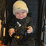 baby, child, stroller, hat, knit_hat, clothing, smile, face, blue_eyes, seat_belt, black_clothing, indoor, baby_clothes, infant, cute, person, mickey_mouse, happy, sitting, young_child