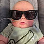 Weston is registered to the contest to win money with this photo: baby, child, sunglasses, green_shirt, striped_clothing, nasal_tube, infant, cute, face, chubby_cheeks, cushion, seat, portrait, indoor, person, young_child, headwear, cool, fashion, medical_tube