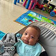 Jésaiah a rejoint le concours — aidez-le/la à gagner de superbes lots ! baby, infant, cute, playmat, toys, pacifier, seat, blue_bib, gray_clothing, floor, indoor, child, smiling, tongue_out, colorful, playroom, young_child, baby_boy, comfortable, happy