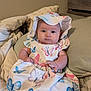 baby, infant, child, dress, hat, butterfly_pattern, bed, pillow, blanket, indoors, cute, chubby_cheeks, sitting, clothing, person, portrait, young_child, soft_lighting, comfortable, curious