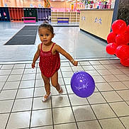 Janae joined the competition — help win amazing prizes! toddler, child, balloon, indoor, red_clothing, purple_balloon, tiles, floor, lockers, counter, red_balloons, bracelet, shoes, person, walk, young_child, hair_bun, toy_store, lighting, smile
