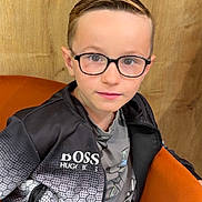 Sacha a rejoint le concours — aidez-le/la à gagner de superbes lots ! child, boy, glasses, jacket, sitting, chair, wooden_background, orange_chair, casual_clothing, portrait, indoor, young, face, person, fashion, confident, short_hair, black_jacket, grey_shirt, zipper