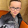 child, boy, glasses, jacket, sitting, chair, wooden_background, orange_chair, casual_clothing, portrait, indoor, young, face, person, fashion, confident, short_hair, black_jacket, grey_shirt, zipper