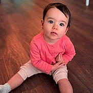 Alice is registered to the contest to win money with this photo: child, toddler, indoor, floor, wooden_floor, pink_clothing, socks, sitting, looking_up, curious, portrait, baby, person, cute, long_sleeve, casual, home, young_child, innocent, expression