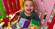 Gabriel joined the competition — help win amazing prizes! baby, child, smiling, laughing, sitting, playpen, toys, blocks, colorful, indoor, portrait, happy, infant, doll, play_mat, socks, clothing, wooden_floor, playroom, face