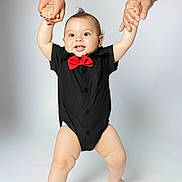 Gabriel is registered to the contest to win money with this photo: baby, child, infant, smiling, portrait, studio, bow_tie, black_outfit, red, adult_hands, being_held, standing, arms_raised, happy, face, indoor, white_background, fashion, family, photography