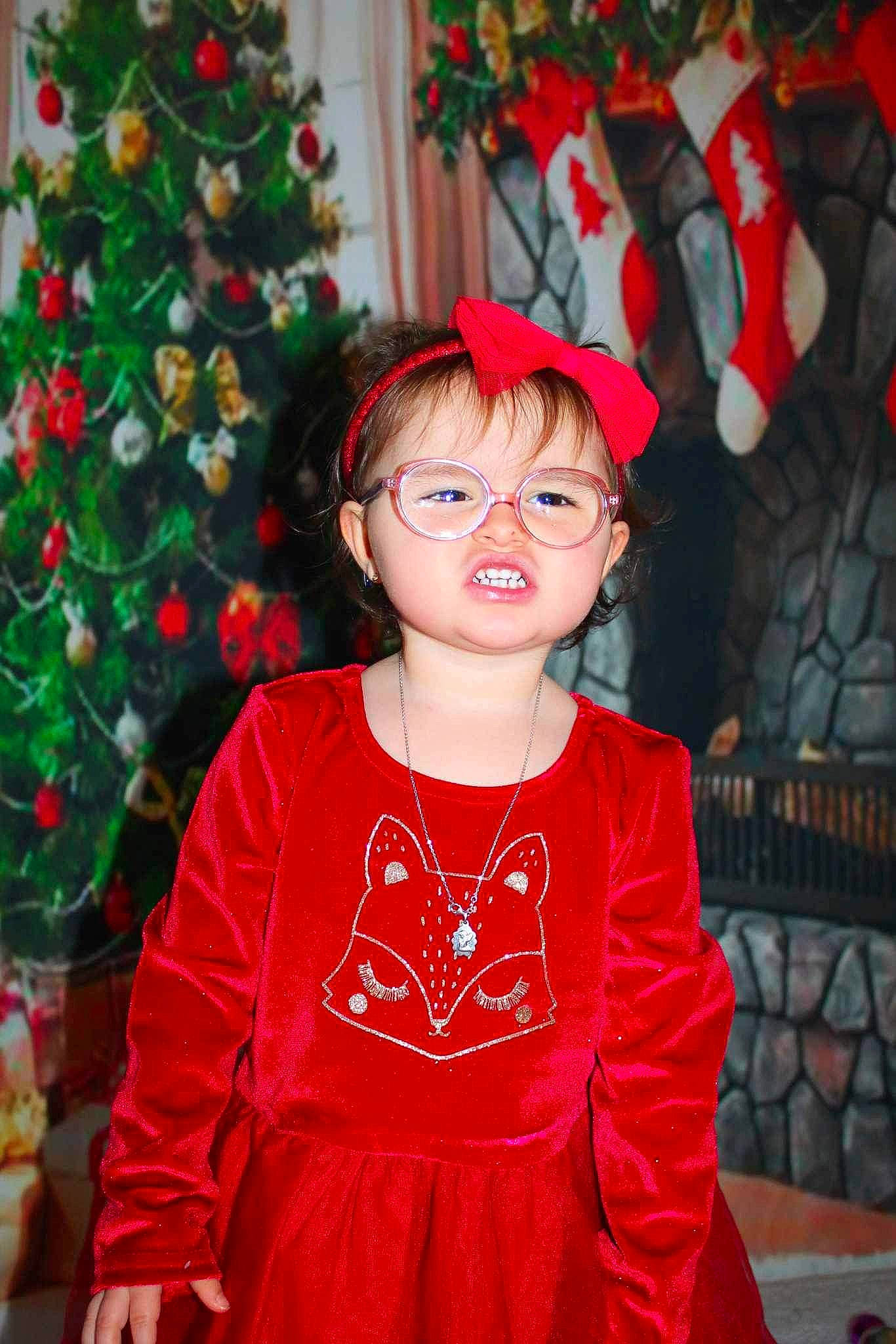 Illyana participe au concours pour gagner de l'argent avec cette photo : baby_toddler_clothing, christmas_ornament, christmas_tree, dress, embellishment, eye, facial_expression, fun, glasses, hair, happy, head, holiday_ornament, human_body, person, plant, red, sleeve, smile, toddler