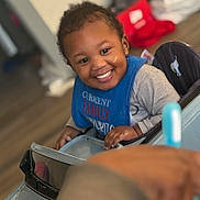 Karzoo joined the competition — help win amazing prizes! bib, blue_bib, child, clothing, cute, expression, face, floor, furniture, hand, happy, human, indoor, person, play, seat, smiling, toddler, toy_car, young_child