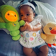 Amelia is registered to the contest to win money with this photo: baby, child, plush_toy, green_toy, yellow_duck, bed, white_headband, floral_clothing, hand, indoor, cute, infant, soft_toy, colorful, lying_down, comfort, person, portrait, expression, cozy