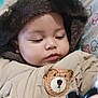 baby, child, jacket, hood, bear_patch, toy, blanket, face, person, indoor, warm_clothing, cute, infant, closeup, soft_texture, childhood, expression, seated, colorful, pattern
