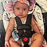 baby, child, car_seat, headband, floral_pattern, straps, sitting, infant, seatbelt, cute, serious_expression, indoor, closeup, person, colorful, soft_fabric, comfort, small_child, portrait, seat